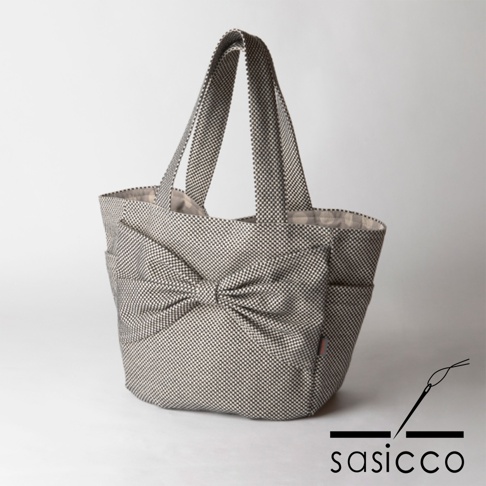 以三河木綿刺子織材質製成的托特包，採用經典的千鳥格紋圖案，正面裝飾有立體蝴蝶結，搭配雙提把設計，展現簡約優雅風格。