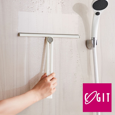白色刮水器，帶有灰色橡膠刮條，可旋轉折疊手柄，正在清潔帶有泡沫的玻璃表面。旁邊是掛在牆上的白色淋浴噴頭。