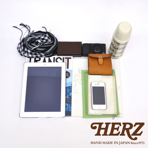 黑白格紋圍巾、深棕色皮夾、黑色相機、棕色皮革零錢包，以及白色平板電腦、書籍、手機和保溫瓶。