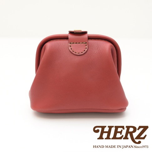 酒紅色皮革口金化妝包，中間有皮革束帶和金屬釦，邊緣有縫線裝飾。