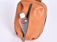 職人手作皮革立體運動斜背包 (F-9)，採用淺棕色皮革材質，包身呈現圓潤立體造型，一側設有拉鍊開口，可放入一瓶透明塑膠瓶裝水。