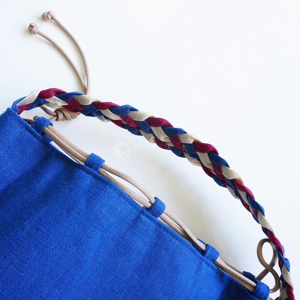 BAN INOUE 麻花辮束口手提包，藍色帆布包身搭配編織提把，提把由米白色、藍色和紅色線編織而成，細節處可見麻繩穿過帆布環。