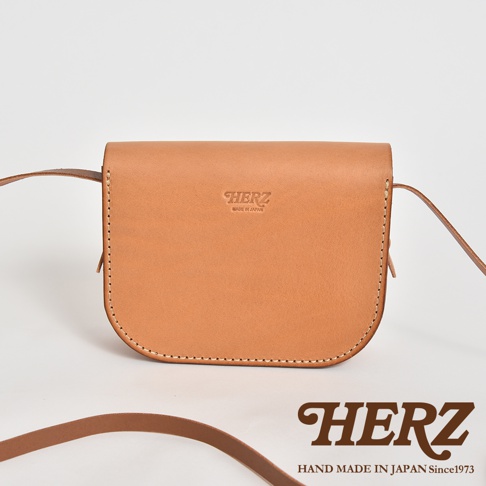 淺棕色職人手作皮革流蘇側背包，簡約設計，帶有品牌燙金標誌。包包採用柔軟皮革製成，縫線清晰，配有可調節的長肩帶。