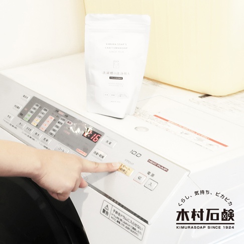 白色軟管包裝的滾筒洗衣機專用清潔粉，置於白色洗衣機面板上方。面板上有數字顯示、按鈕及日文說明。