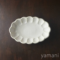 一個白色、帶有花瓣狀邊緣的橢圓形陶瓷料理盤，盤面中央平坦，邊緣有手工製作的紋理感。