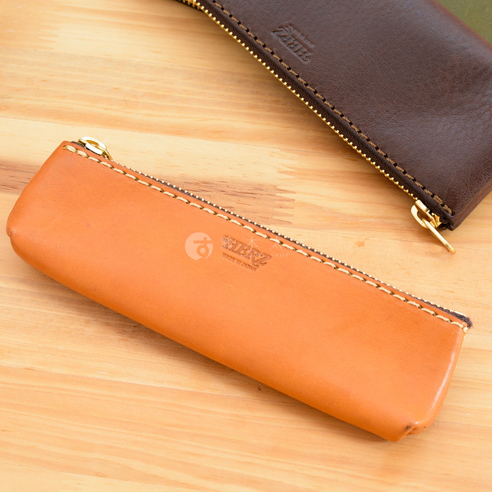 職人手作皮革經典收納筆袋，一個為橘棕色皮革，另一個為深棕色皮革，兩者皆有金色拉鍊和縫線細節，皮革表面印有品牌Logo。