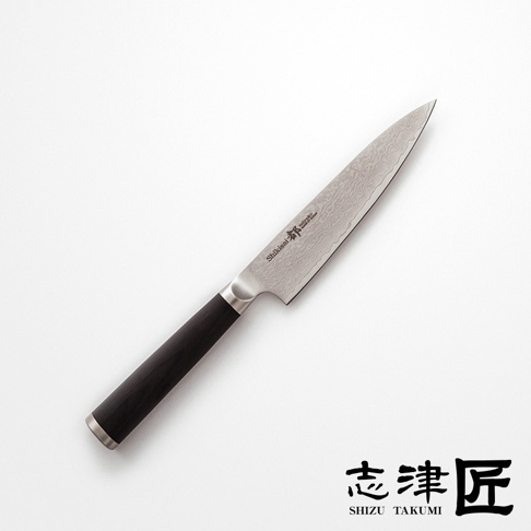 一張俯視圖，顯示一把黑色刀柄、銀色刀刃的廚刀，刀刃上印有「Shikisai 」，刀刃有大馬士革紋路。右下角有「志津匠 SHIZU TAKUMI」的黑色標誌。