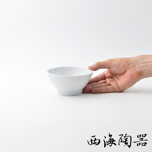 一只手托著一個白色陶瓷飯碗，碗身呈圓弧形，底部有微微的縮口。