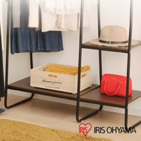 黑色金屬框架搭配木紋層板的吊掛衣架，展示有藍色洋裝、針織衫、木質收納盒（內含黃色毛毯）及紅色手提包，上方層板放置一頂米色寬邊帽。