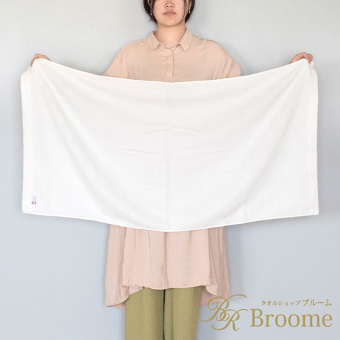 一位女士展開一條白色、純棉、帶有菱形紋理的長浴巾。浴巾左側有一個小標籤。