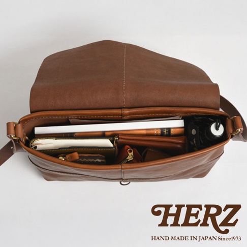 日本HERZ職人手作皮革細扣帶馬鞍包，展示打開的包內部裝有書籍、錢包、記事本及雨傘等物品。