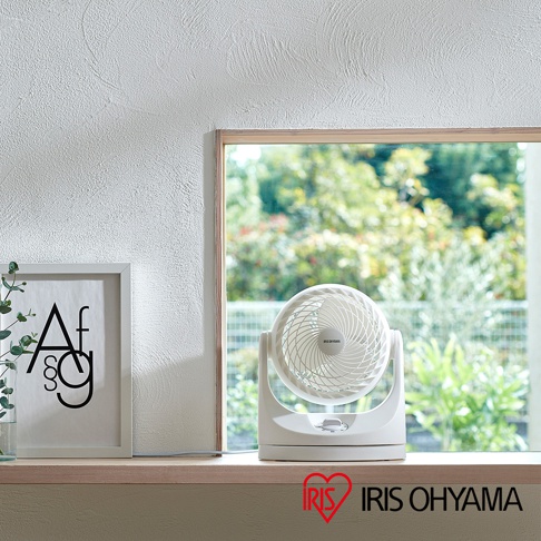 白色IRIS OHYAMA PCF-MKM15空氣循環扇，具有可調節角度的圓形扇頭，置於窗邊木質檯面上。