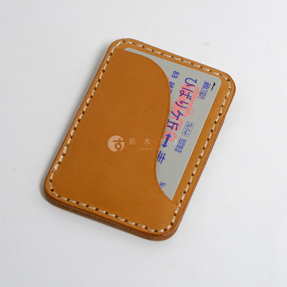 一個淺棕色的皮革名片夾，上面縫有米白色的線跡，夾內露出一張帶有日文文字的卡片。