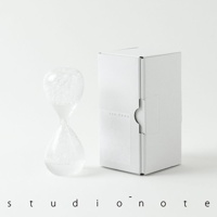 awaglass 泡時計，由透明玻璃製成，中間收窄，上下兩端為球狀。頂部球體內充滿白色泡沫，底部球體內也聚集了白色泡沫。產品旁有一個白色的紙盒，盒身上印有「awaglass」字樣和蜂巢圖案。