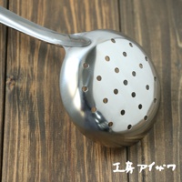 一個不鏽鋼中型撈勺，勺面帶有許多圓形孔洞，勺柄光滑，置於木紋背景上。