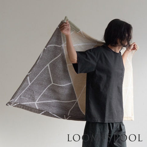 一位男子身穿黑色短袖上衣和褲子，展開一條印有幾何圖案的淺棕色與深灰色相間的毛巾。