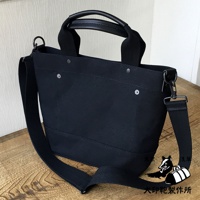 黑色帆布兩用托特包，附有皮革提把與可拆卸的帆布肩背帶，包身綴有金屬鉚釘。