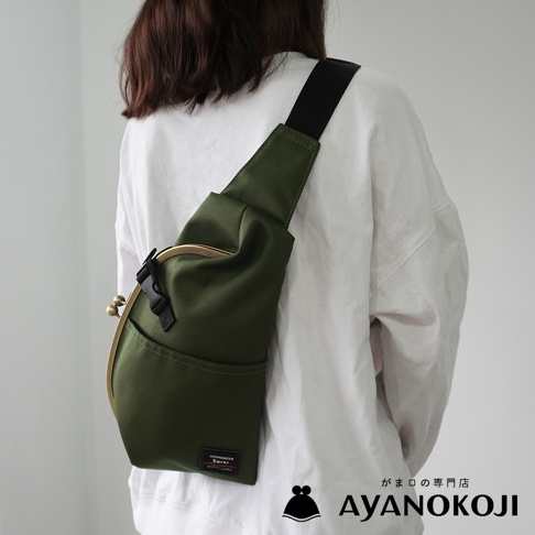 一位女士身穿白色上衣，斜挎一個綠色布質口金斜背包，包包上有一個金屬框架和一個黑色扣環。