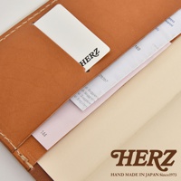 HERZ 品牌標誌在深棕色皮革手帳書套上，書套有縫線細節，並可見標籤。