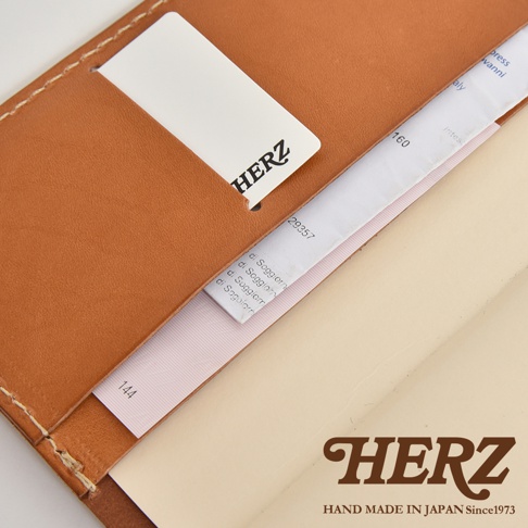HERZ 品牌標誌在深棕色皮革手帳書套上，書套有縫線細節，並可見標籤。