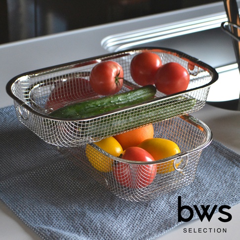 兩個簡約不鏽鋼瀝水籃，上方籃子裝有番茄和黃瓜，下方籃子裝有柑橘、檸檬和番茄，均置於淺灰色織物墊上。