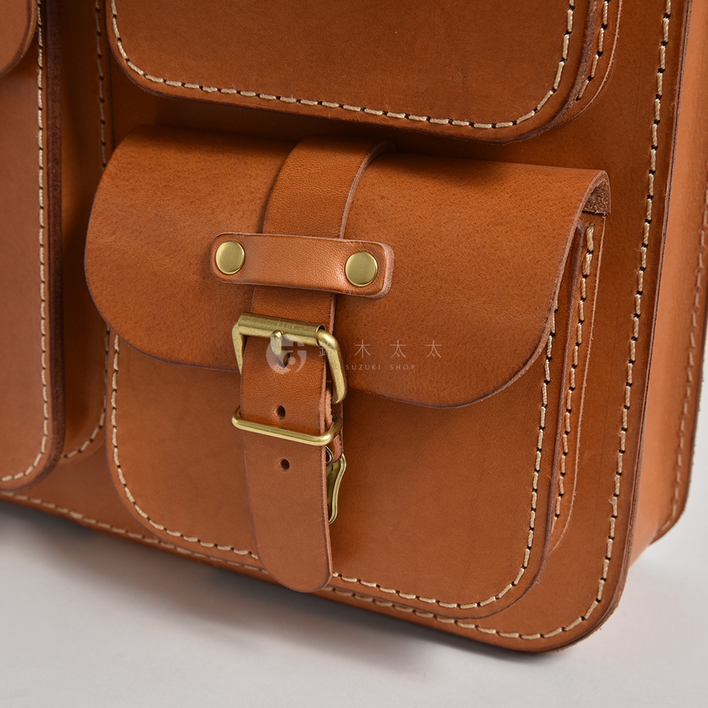 職人手作皮革後背包，採用鞣製棕色皮革，有雙層口袋設計，中央口袋以皮革束帶及黃銅扣環固定，車縫線明顯。