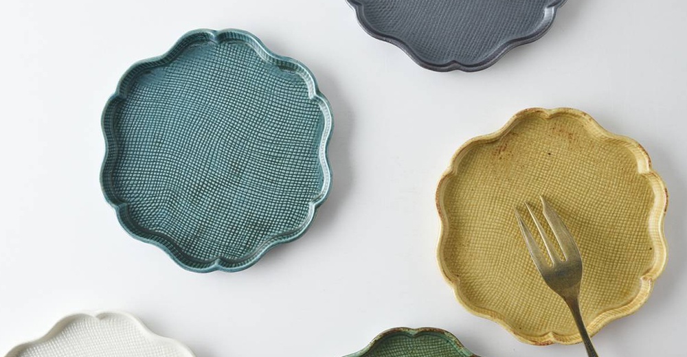 美濃燒花型甜點盤，表面有細緻的編織紋理。盤子邊緣呈花瓣狀，共有藍綠色、黃色、灰色、白色和綠色等多種顏色。