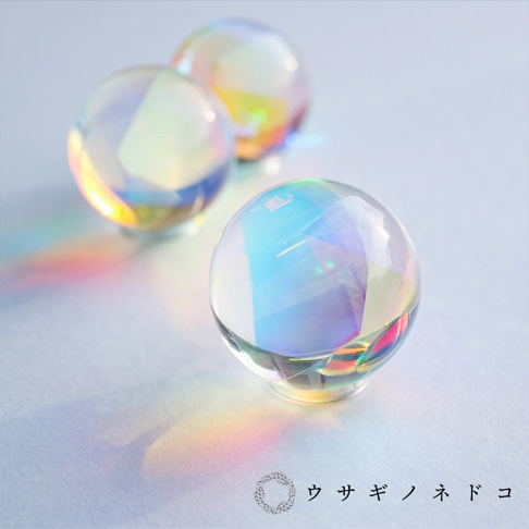 三個透明的玻璃稜鏡球，表面有切割面，折射出彩虹般的光芒，散落在淺藍色背景上。