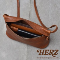 一個棕褐色的皮革斜背包，裡面裝著一個錢包和一個黑色皮夾，包包敞開著，露出拉鍊內袋。