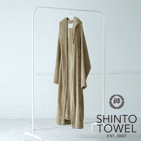 一件淺棕色、連帽、長袖的蓬厚浴袍，懸掛在白色衣架上，材質看起來柔軟舒適。