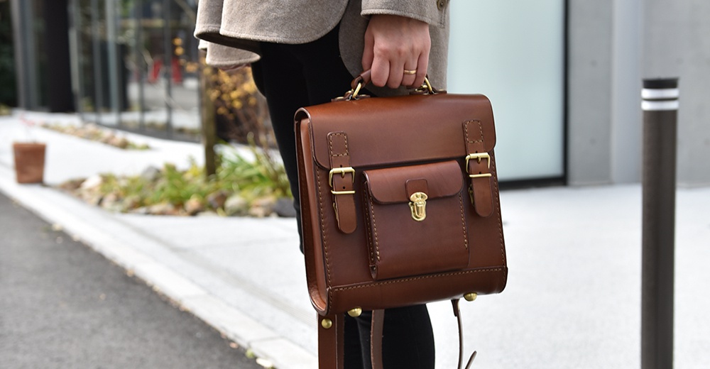 職人手作皮革經典學院風迷你後背包，採用光滑棕色皮革製成，配有黃銅色金屬扣環和鎖頭。