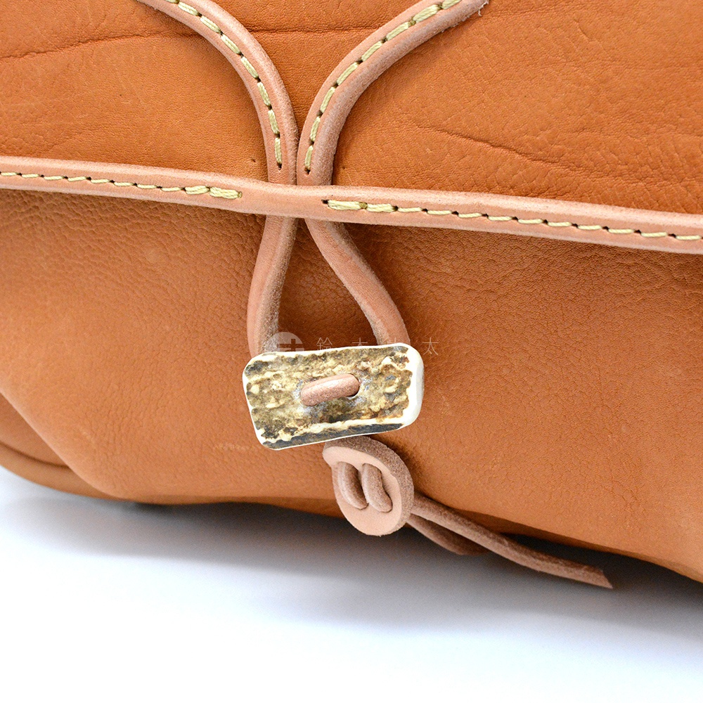 棕褐色皮革郵差包，採用鹿角和皮革繩作為閉合設計，縫線精緻。