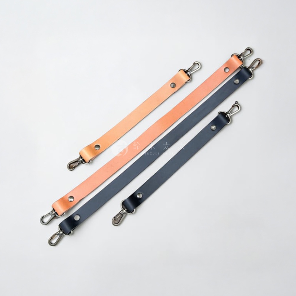 這張照片展示了三條皮革短提帶，分別為兩條淺棕色與兩條深藍色，均配置了金屬扣環與固定鉚釘，排放在白色背景上。