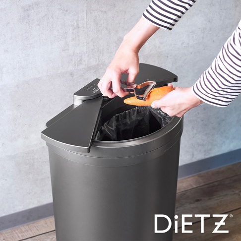 灰色30公升DustBox30自動感應靜音垃圾桶，頂部設有兩個可開合的蓋子，一人手持削皮器正在將胡蘿蔔放入垃圾桶內。