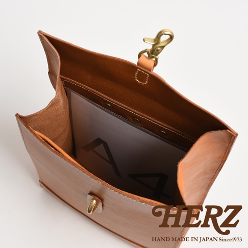 職人手作皮革紙袋風後背包，呈現原色皮革質地，包含一個金屬扣環及一個固定帶。內部可見A4文件夾。