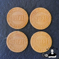 四塊圓形、金黃色的薄餅，表面印有「GAUFRE」字樣及葉片狀的裝飾紋路，擺放在深色背景上。