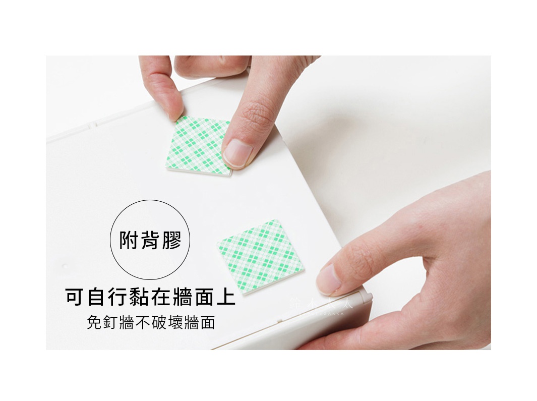 兩隻手正在將白色帶有綠色格紋的雙面膠貼黏在一個白色產品的角落，此產品應為加深型ABS壁掛/桌上兩用擦手紙架。