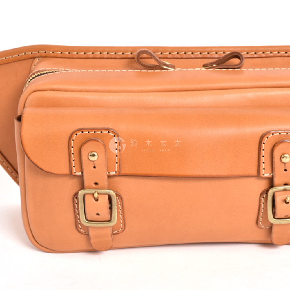 淺棕色皮革騎士隨身斜背包，設有雙扣帶翻蓋、拉鍊開合和兩個皮革拉袢。