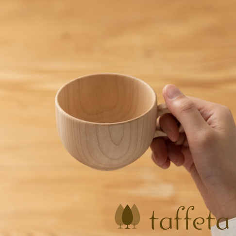 手持淺色楓木製茶杯，杯身圓潤，木紋清晰，搭配簡約木質背景。