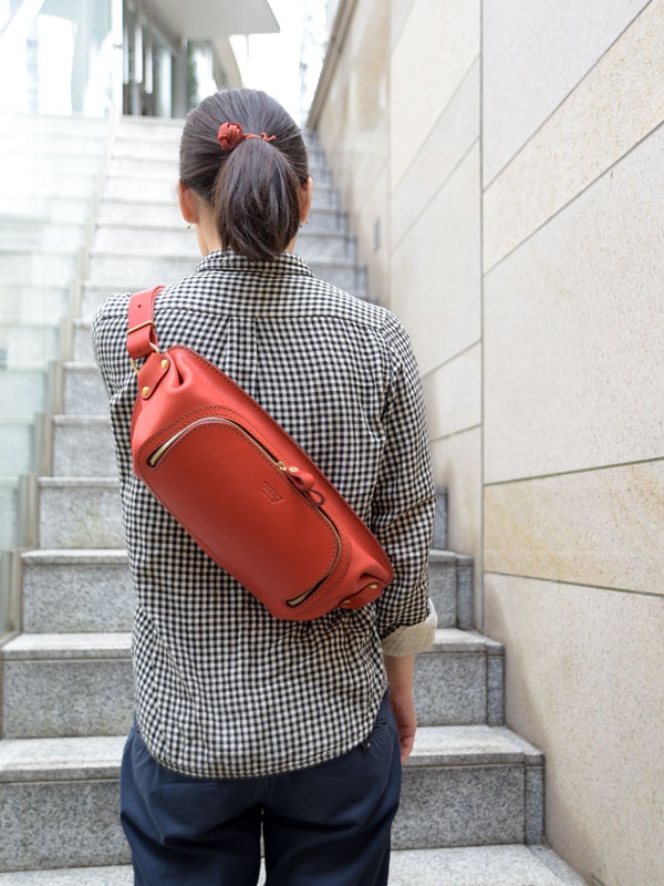 紅色皮革拉鍊斜背包，側面有拉鍊設計，肩帶可調整，包身標有品牌字樣。