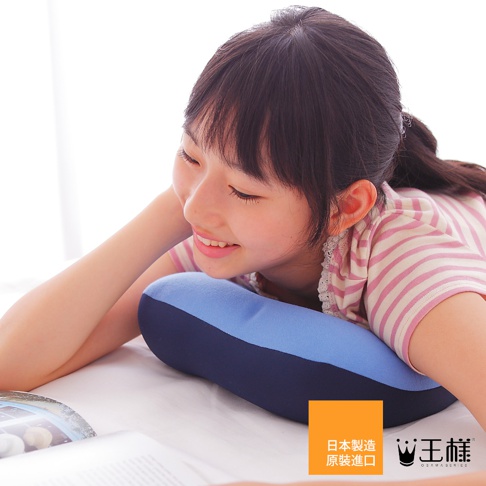 一個女孩趴在床上，臉頰靠在一個藍色和深藍色相間的U型枕上，枕頭材質柔軟，她身上穿著粉色條紋上衣。