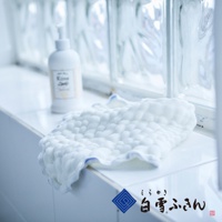 一塊白色的、帶有藍色滾邊的六層紗布洗臉巾，表面有立體紋路，旁邊放著一瓶白色乳液瓶。