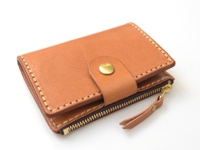 一個棕褐色皮革拉鍊零錢鑰匙包，配有金色壓扣和拉鍊，以及皮革拉鍊繩。包包邊緣有白色縫線。