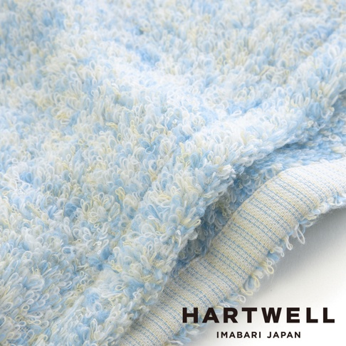 這是一張 HARTWELL 今治毛巾的細節特寫，畫面呈現充滿質感的藍白黃混色長毛圈織法，毛巾邊緣露出精緻的收邊細節，整體色調柔和，品牌 HARTWELL IMABARI JAPAN 字樣位於右下角。