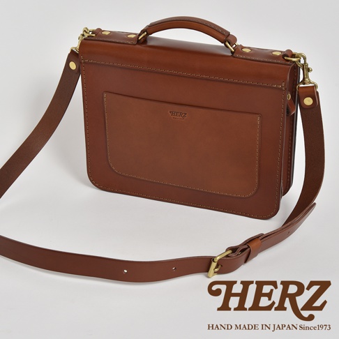 職人手作皮革雙口袋兩用單肩包，以溫潤的棕色皮革製成，包身設有寬大的正面口袋，配有可拆卸的肩帶和頂部提把，整體呈現經典復古風格。