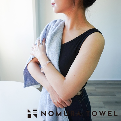 一個女人抱著一條淺藍色毛巾，上面有「NOMURA TOWEL」的標誌