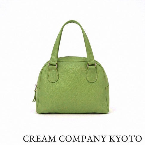 這是一款由 CREAM COMPANY KYOTO 出品的綠色皮革迷你手提包，外觀呈現經典的半月圓弧造型，選用細膩的粒面牛皮製成，整體設計簡約俐落，配有短提把與精緻的拉鍊細節，適合作為日常手提包款使用。