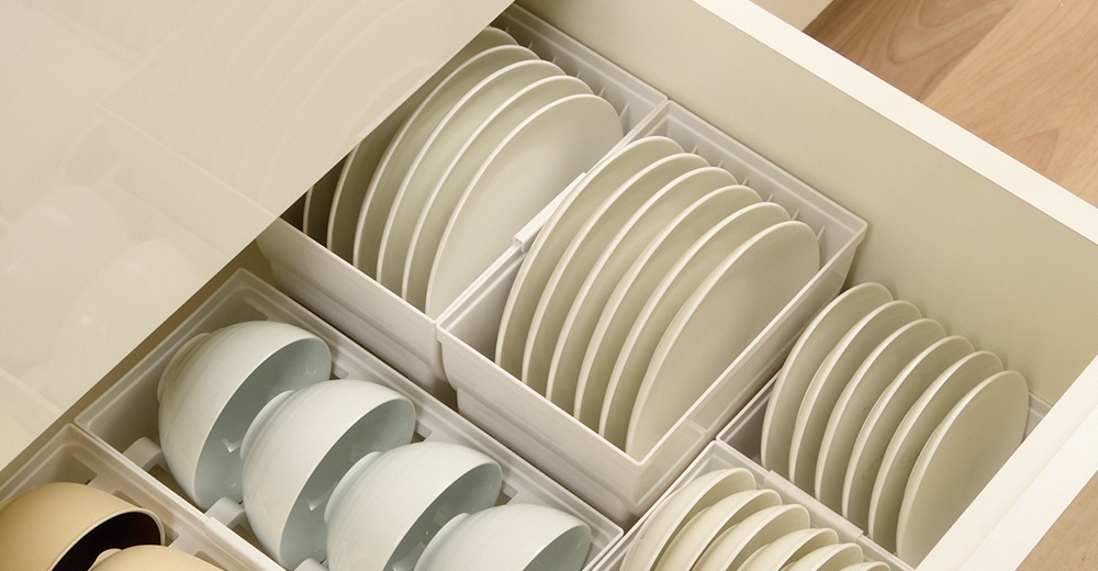 抽屜式餐盤收納架內整齊擺放著數個白色碗盤，盤子垂直放入收納格中，碗則堆疊在另一側的收納格內。