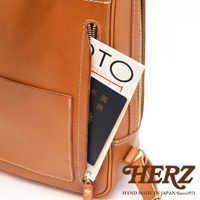 職人手作皮革長方型多口袋後背包，展示部分為淺棕色皮革，側邊拉鍊口袋內插有白色封面、黑色內頁的物品。