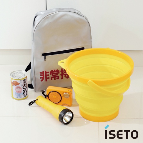 亮黃色伸縮旅行水桶，附有提把，旁邊有銀色背包、橘色收音機、黃色手電筒和一罐食物。
